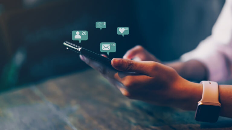 Hände halten ein Smartphone, darüber schweben Benachrichtigungen für Likes, Kontakte und Nachrichten