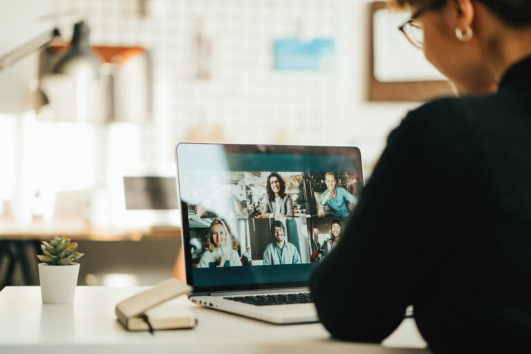 Frau am Schreibtisch in einer Videokonferenz, auf dem Laptop-Bildschirm sind sechs Teilnehmende zu sehen