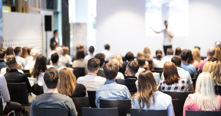 Publikum in einem Konferenzsaal verfolgt den Vortrag eines Redners