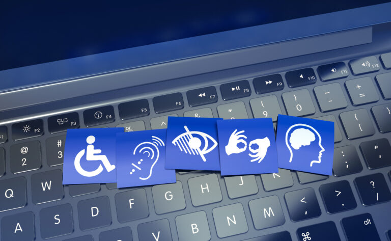 Blaue Karten mit Symbolen für Rollstuhl, Hörbehinderung, Sehbehinderung, Gebärdensprache und kognitive Beeinträchtigung liegen auf einer Laptop-Tastatur